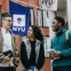 three college students talking and NYU flag in background