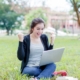 student expressing joy sitting on grass with laptop