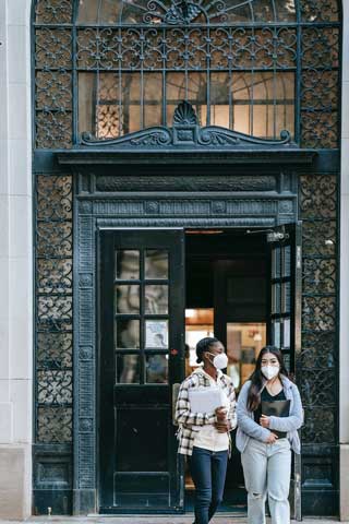 two students walking out of doorway and wearing protective masks